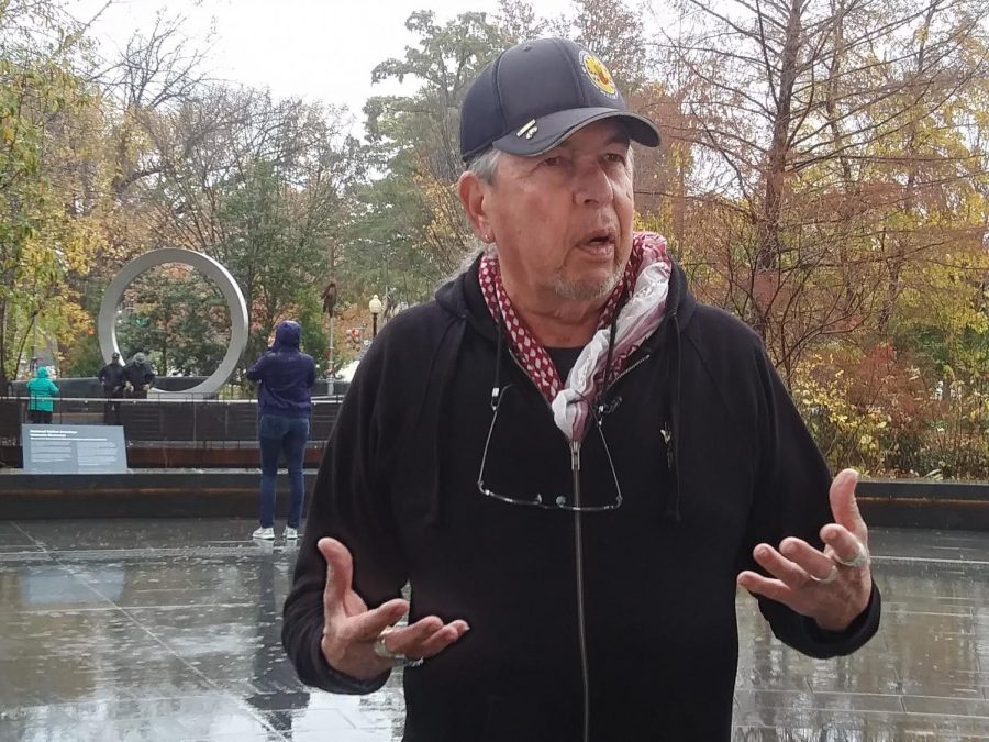 Harvey Pratt, designer of the National Native American Veteran Memorial, speaks with reporters at the Museum of the American Indian. The memorial can be seen in the distance over his shoulder. Photo courtesy Gaylord News / Jessie Christopher Smith