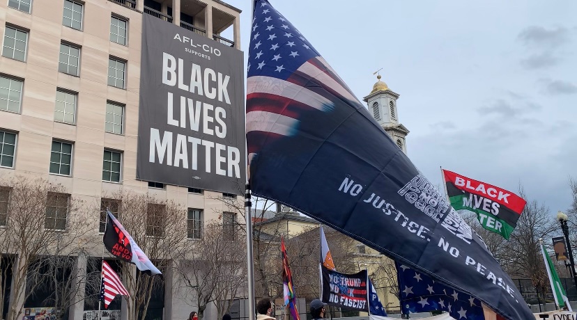 BLM protestors hold flags up against the fence protecting the White House in Black Lives Matter Plaza. (By Skylar Tallal/Gaylord News)