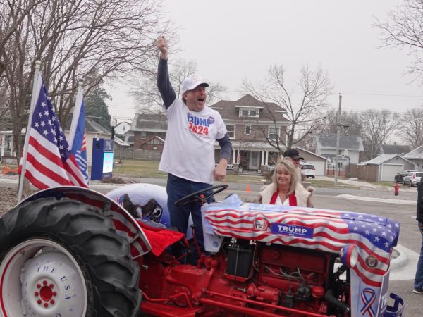 Gary Leffler, Trump Caucus captain, stands on his tractor to excite the crowd outside a rally in Newton, Iowa. Kevin Eagleson/Gaylord News
